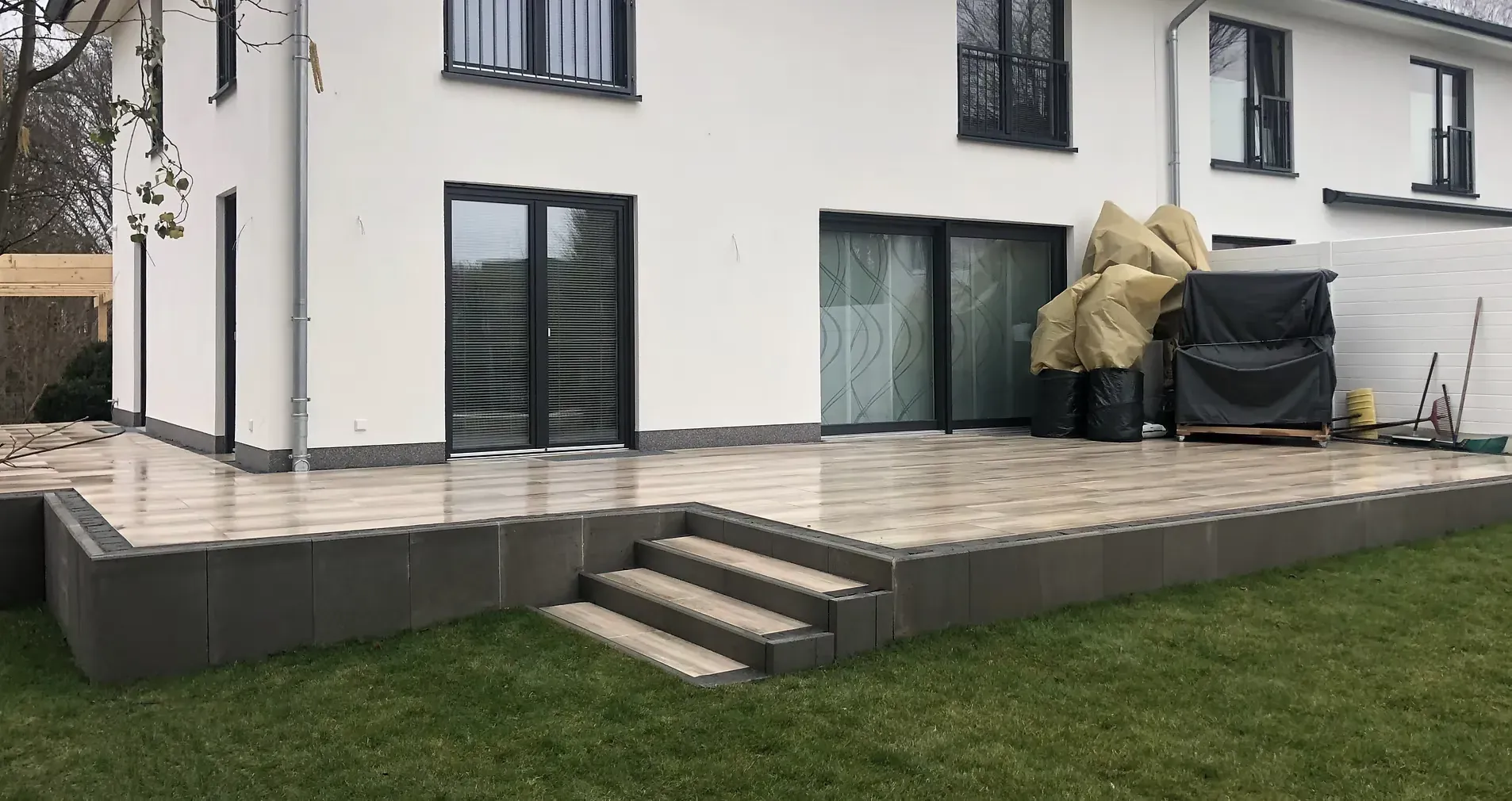 Terrasse aus großformatigen Platten mit Stufenanlage an einem verputzten Wohnhaus.